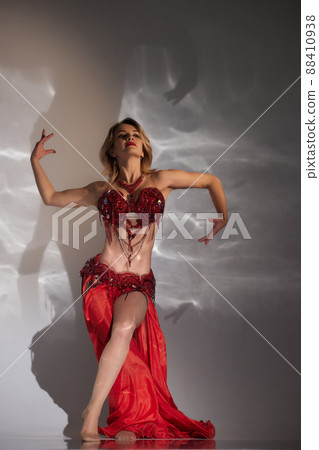 Beautiful girl with long black hair in a red oriental dress dancing belly dance in the studio room. Arab culture. 88410938