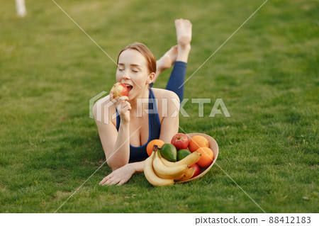 Woman in a garden. Lady with a fruits. Girl in a sportwear. 88412183