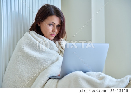 Woman warming with blanket heating radiator, using laptop. Woman warming with blanket heating radiator, using laptop. 88413136
