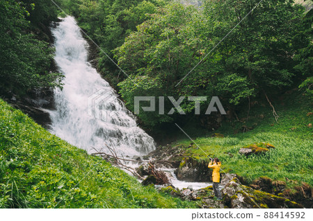 Gudvangen-Naeroyfjorden, Norway. Waterfall Tuftofossen In Spring. Natural Norwegian Landmark. Young Caucasian Woman Lady Tourist Traveler Photographer Taking Pictures Of Tuftefossen Waterfall 88414592