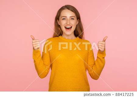 Thumbs up. Portrait of attractive cheerful ginger girl in sweater doing like gesture with finger up, expressing approval, customer showing excellent feedback. studio shot isolated on pink background 88417225