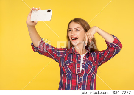 Look down, subscribe. Portrait of cheerful girl blogger in casual shirt making video call or online streaming using mobile phone, pointing finger down, asking to follow social media. studio shot 88417227