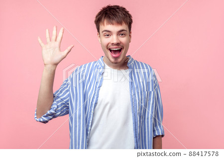 Hi, Hello. Portrait of happy friendly brown-haired man with small beard and mustache in casual shirt waving hand to camera, welcoming with toothy smile. indoor studio shot isolated on pink background Hi, Hello. Portrait of happy friendly brown-haired man with small beard and mustache in casual shirt waving hand to camera, welcoming with toothy smile. indoor studio shot isolated on pink background 88417578