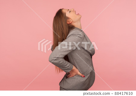 Portrait of ill young woman in business suit feeling unhealthy, touching back and shouting from pain, suffering back ache, having discomfort lower lumbar muscular, kidney stones. studio shot, isolated Portrait of ill young woman in business suit feeling unhealthy, touching back and shouting from pain, suffering back ache, having discomfort lower lumbar muscular, kidney stones. studio shot, isolated 88417610