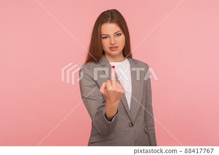 Portrait of irritated young woman in business suit showing middle finger, impolite rude gesture of disrespect, expressing hate and aggression in conflict. studio shot isolated on pink background 88417767