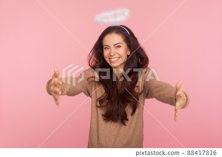 Angelic kindness and generosity. Portrait of beautiful young woman with halo above head holding outstretched hands and smiling, giving free hugs, inviting to embrace. indoor studio shot, isolated 88417816