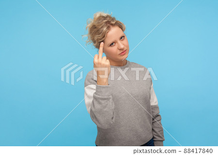 Impolite angry woman with short curly hair in casual sweatshirt showing fuck sign with middle finger, rude gesture of disrespect, fuck off expression. indoor studio shot isolated on blue background 88417840