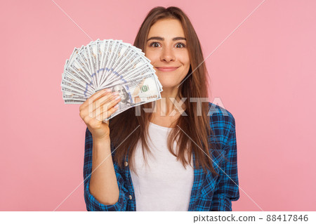 Portrait of happy lucky girl in checkered shirt holding lot of money and smiling to camera, showing dollar bills in hand, enjoying financial success. indoor studio shot isolated on pink background Portrait of happy lucky girl in checkered shirt holding lot of money and smiling to camera, showing dollar bills in hand, enjoying financial success. indoor studio shot isolated on pink background 88417846