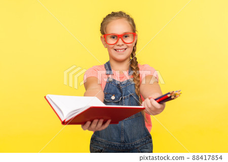 Portrait of clever creative little girl in red glasses holding notebook and pencils, school child smiling at camera showing homework, education concept. studio shot isolated on yellow background 88417854