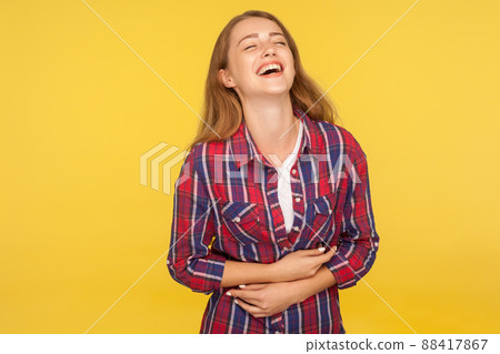 Portrait of carefree ginger girl in checkered shirt holding belly and laughing out loud after hearing hilarious joke, funny anecdote, being in good mood. studio shot isolated on yellow background Portrait of carefree ginger girl in checkered shirt holding belly and laughing out loud after hearing hilarious joke, funny anecdote, being in good mood. studio shot isolated on yellow background 88417867