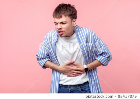 Stomach ache. Portrait of sick brown-haired man with small beard and mustache in casual shirt touching belly suffering abdominal pain, gastritis or constipation. indoor, isolated on pink background 88417879