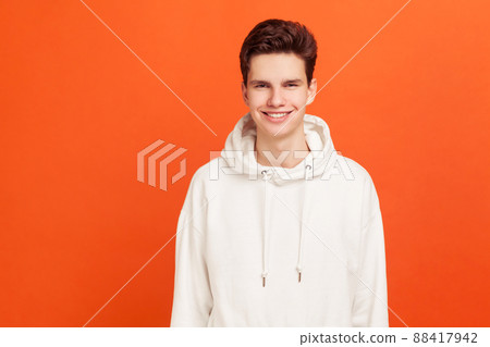 Smiling teenager in hoody looking at camera, positive and successful male person. Happy youth. Indoor studio shot isolated on orange background 88417942