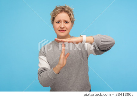 Frustrated woman with short curly hair in grey sweatshirt feeling tired and overworked, showing timeout gesture, need more time, missing deadline. indoor studio shot isolated on blue background Frustrated woman with short curly hair in grey sweatshirt feeling tired and overworked, showing timeout gesture, need more time, missing deadline. indoor studio shot isolated on blue background 88418003