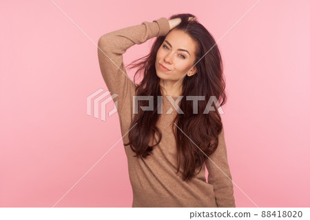 Portrait of stunning sexy slim woman in casual pullover touching her long brunette wavy hair and looking at camera with alluring eyes, fashion and beauty concept. indoor studio shot, pink background Portrait of stunning sexy slim woman in casual pullover touching her long brunette wavy hair and looking at camera with alluring eyes, fashion and beauty concept. indoor studio shot, pink background 88418020