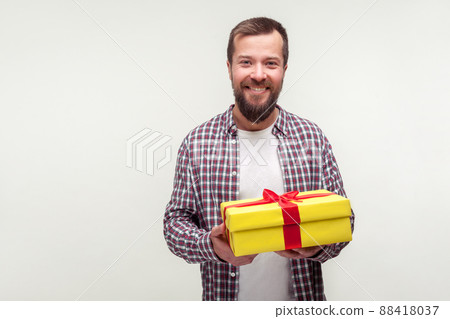 Portrait of happy satisfied bearded man in casual plaid shirt holding gift box and smiling at camera, enjoying holiday celebration with present. indoor studio shot isolated on white background 88418037