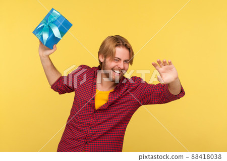 Happy carefree man in checkered shirt holding gift ready to throw box, congratulating close friend, laughing and having fun, tossing around present. indoor studio shot isolated on yellow background Happy carefree man in checkered shirt holding gift ready to throw box, congratulating close friend, laughing and having fun, tossing around present. indoor studio shot isolated on yellow background 88418038