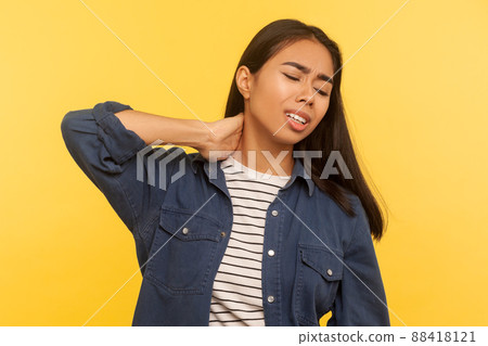 Tired overworked girl feeling unwell, rubbing her neck and grimacing from pain, suffering muscle tension, problem with spine, hurting shoulders. indoor studio shot isolated on yellow background Tired overworked girl feeling unwell, rubbing her neck and grimacing from pain, suffering muscle tension, problem with spine, hurting shoulders. indoor studio shot isolated on yellow background 88418121