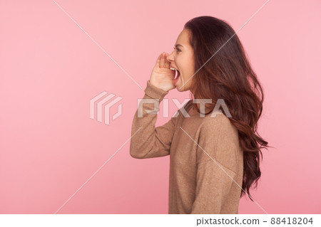 Attention, important message. Side view of young woman with brunette wavy hair shouting news or proclaiming idea with hand near mouth, announcing advertisement. studio shot isolated on pink background Attention, important message. Side view of young woman with brunette wavy hair shouting news or proclaiming idea with hand near mouth, announcing advertisement. studio shot isolated on pink background 88418204