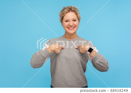 This is me. Happy egoistic woman with short curly hair in sweatshirt pointing herself and smiling at camera, proud of personal achievements, success. indoor studio shot isolated on blue background This is me. Happy egoistic woman with short curly hair in sweatshirt pointing herself and smiling at camera, proud of personal achievements, success. indoor studio shot isolated on blue background 88418249