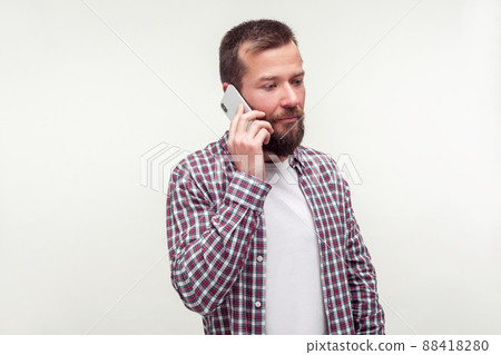 Portrait of serious upset bearded man in plaid shirt talking on cell phone, looking aside with gloomy dismal face, bad news, mobile communication. indoor studio shot isolated on white background 88418280