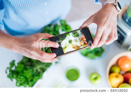 Blogger creating content for social media. Woman making photo, video with just made glass of detox green smoothie and it's ingredients on the kitchen table. Healthy dieting, cooking, weight loss blog. 88418692