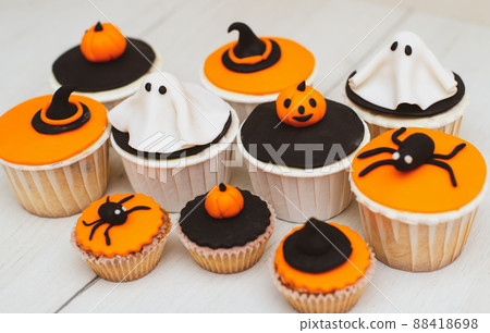 Halloween muffins with decorations in the form of ghosts, pumpkins and witch hats. A set of festive cupcakes and treats for a Halloween party Halloween muffins with decorations in the form of ghosts, pumpkins and witch hats. A set of festive cupcakes and treats for a Halloween party 88418698