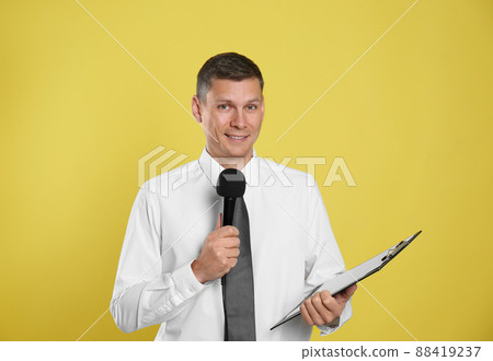 Male journalist with microphone and clipboard on yellow background Male journalist with microphone and clipboard on yellow background 88419237