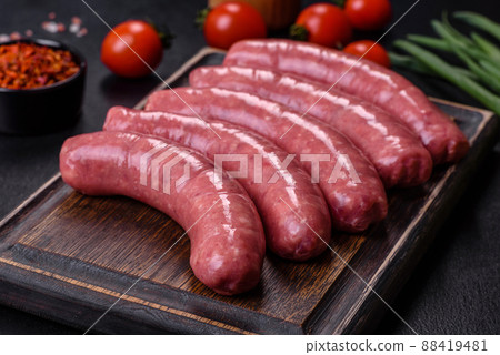 Raw sausages with ingredients on a cutting board on a stone background with copy space Raw sausages with ingredients on a cutting board on a stone background with copy space 88419481