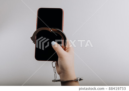 Smartphone chained to handcuff in woman's hand isolated on grey background. Information security or smartphone addiction concept Smartphone chained to handcuff in woman's hand isolated on grey background. Information security or smartphone addiction concept 88419733