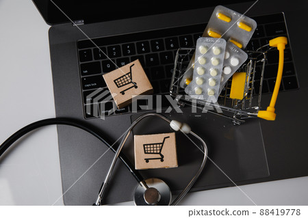 Online pharmacy and delivery drugs concept. Trolley with pills, card boxes and stethoscope on a laptop 88419778