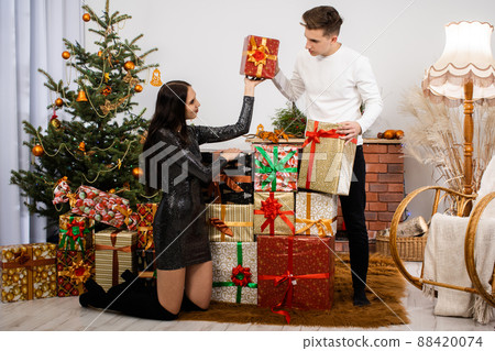 The bride and groom collected a lot of packages with gifts for this year's Christmas. A unique Christmas atmosphere. Shiny black dress. 88420074