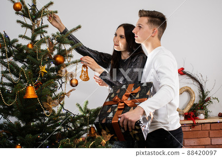Just before the meeting starts, the bride and groom are decorating the Christmas tree at home for Christmas. Christmas decorations. The girl and the boy work together. 88420097