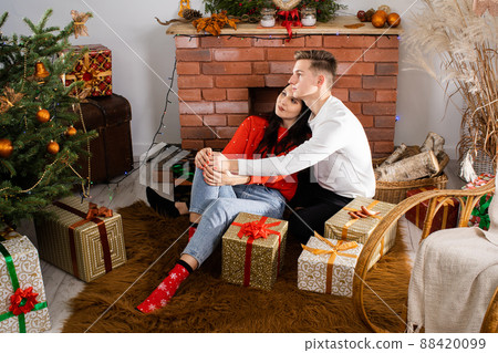 A couple in love are sitting on the floor and flirting. Decorated Christmas tree for Christmas. A unique Christmas atmosphere. 88420099