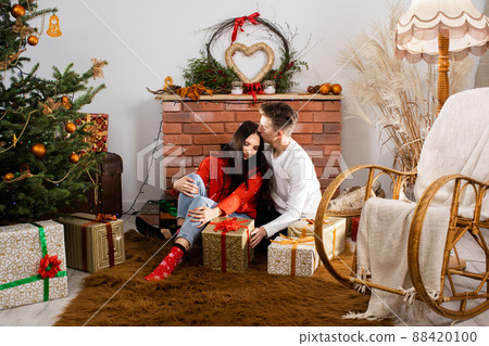 A couple in love are sitting on the floor and flirting. Decorated Christmas tree for Christmas. A unique Christmas atmosphere. 88420100