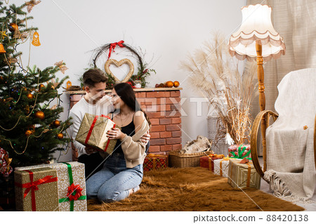 Viewing and arranging gift packages. Couple in love with a gift sits under the Christmas tree. A unique Christmas atmosphere. 88420138