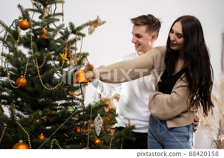 The bride and groom are decorating the Christmas tree at home for Christmas. Christmas decorations. The girl and the boy work together. 88420158