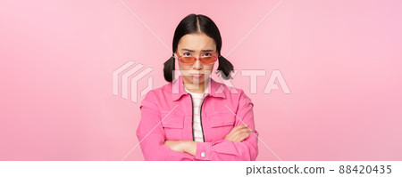 Portrait of sad and gloomy asian girl sulking from disappointment, standing upset against pink studio background Portrait of sad and gloomy asian girl sulking from disappointment, standing upset against pink studio background 88420435