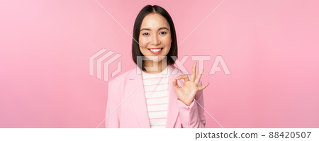 Excellent work, well done gesture. Smiling asian businesswoman showing okay, ok sign, praise good work, recommending company, looking as confident professional, pink background 88420507