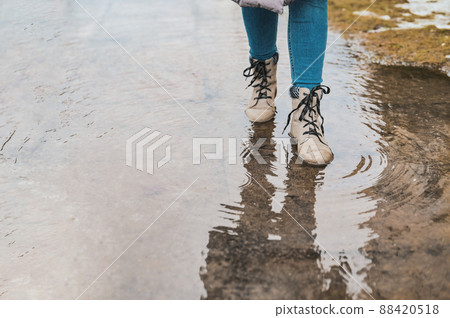 A woman steps into a puddle. Splashes of water scatter from under the feet. A woman steps into a puddle. Splashes of water scatter from under the feet. 88420518