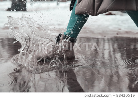 A woman steps into a puddle. Splashes of water scatter from under the feet. A woman steps into a puddle. Splashes of water scatter from under the feet. 88420519