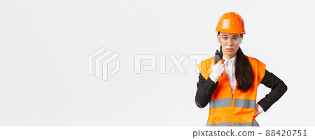 Disappointed asian female construction engineer, technician or industrial manager in safety uniform calling employee via walkie-talkie, scolding personal using radio communication at enterprise 88420751
