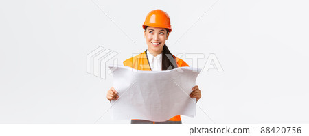 Creative asian female architect imaging her plan, standing in safety helmet and looking away thoughtful while reading blueprints, picturing buiding after finish construction works, white background Creative asian female architect imaging her plan, standing in safety helmet and looking away thoughtful while reading blueprints, picturing buiding after finish construction works, white background 88420756