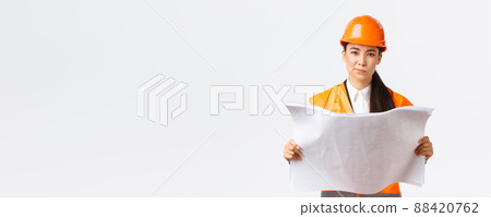 Thoughtful professional asian female construction manager, architect reading blueprints and looking at camera pondering, making decision while studying project plan, white background Thoughtful professional asian female construction manager, architect reading blueprints and looking at camera pondering, making decision while studying project plan, white background 88420762