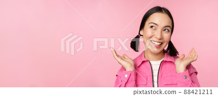 Skin care and cosmetology concept. Beautiful asian girl smiling and laughing, showing clean healthy facial skin, posing against pink background 88421211