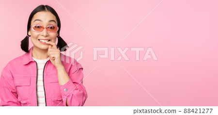 Stylish asian girl in sunglasses, looks thoughtful or intrigued, wants to try smth out, stands over pink background, pondering Stylish asian girl in sunglasses, looks thoughtful or intrigued, wants to try smth out, stands over pink background, pondering 88421277