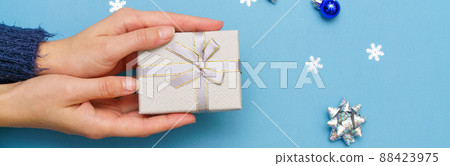 Woman's hands holding gift box present, tied with ribbon bow on blue background 88423975