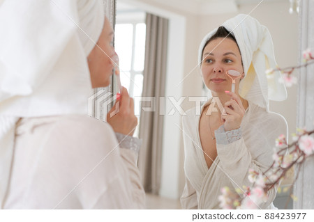 Portrait woman wrapped in white towel and in bathrobe looks at reflection 88423977