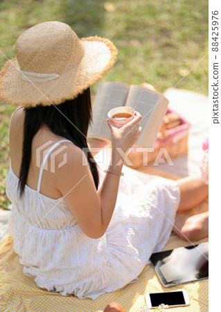 Pretty girl reading a book and sipping tea while having a picnic in the garden. 88425976