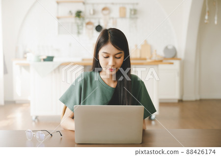 Smiling asian young woman working on laptop at home office 88426174