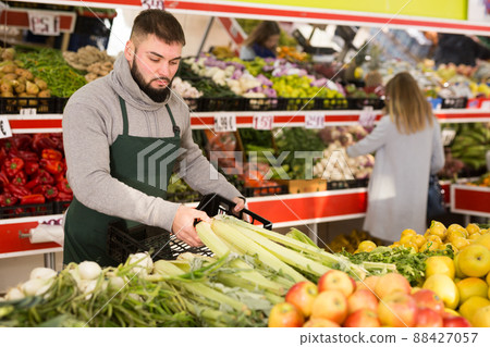 Shopping assistant puts vegetables and fruits on supermarket counter Shopping assistant puts vegetables and fruits on supermarket counter 88427057